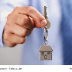 Holding out house keys on a house shaped keychain