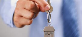 Holding out house keys on a house shaped keychain