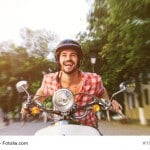 Smiling handsome young man riding scooter