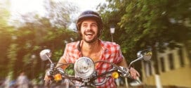 Smiling handsome young man riding scooter