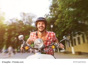 Smiling handsome young man riding scooter